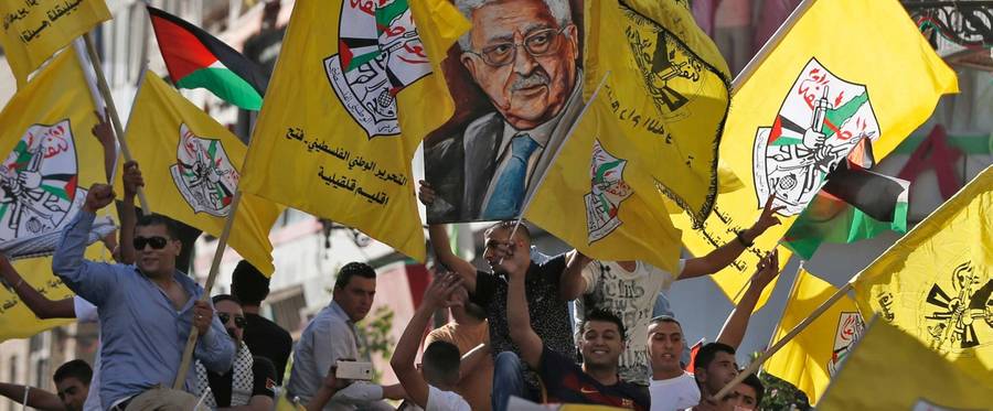 Palestinians supporting the Fatah movement wave both their national and the movement's flags as they take part in a demonstration in the West Bank city of Ramallah on October 4, 2016 in support of president Mahmud Abbas' participation in the funeral ceremony of former Israeli President Shimon Peres earlier in the week.