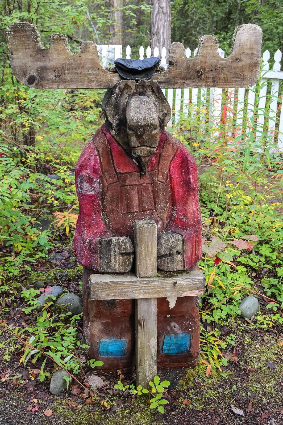 A Wooden Moose sculpture standing behind a cross, in the cemetery at Old St. Nicholas Church in Eklutna