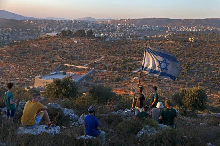 Israeli settler youth lift an Israeli flag in the newly-established wildcat outpost of Eviatar near the northern Palestinian city of Nablus in the West Bank, 2021