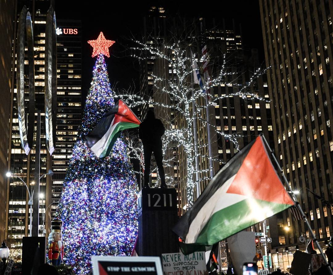 Pro-Palestinian demonstrators, holding flags and banners, gather in front of the illuminated Christmas tree of Rockefeller Center to stage a pro-Palestinian demonstration within the International Day of Solidarity with the Palestinian People in New York, United States on November 29, 2023