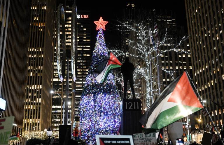 Pro-Palestinian demonstrators, holding flags and banners, gather in front of the illuminated Christmas tree of Rockefeller Center to stage a pro-Palestinian demonstration within the International Day of Solidarity with the Palestinian People in New York City, on Nov. 29, 2023