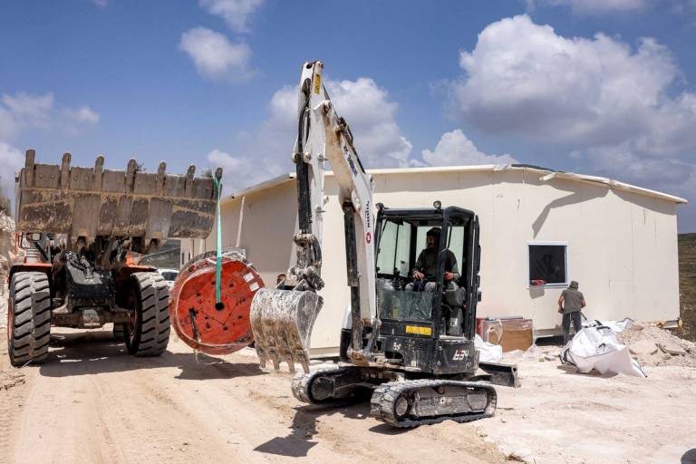An Israeli settler operates an excavator outside a portable building under construction at the former settler outpost of Homesh in the West Bank on May 29, 2023