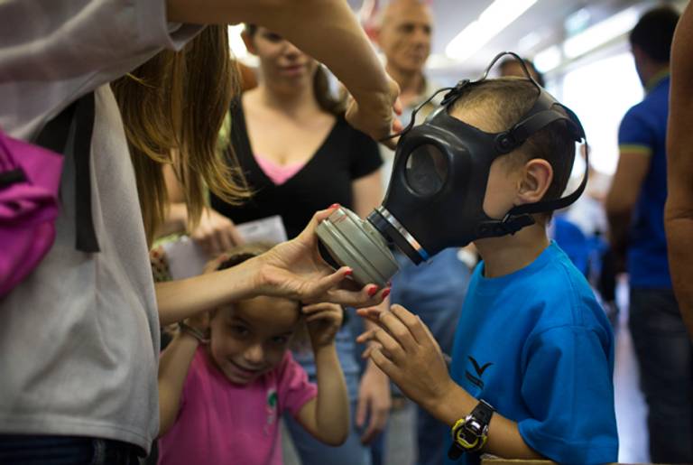 An Israeli woman shows her children how to put on a gas mask as they pick their gas masks at a distribution center on August 26, 2013 in Tel Aviv, Israel.(Uriel Sinai/Getty Images)