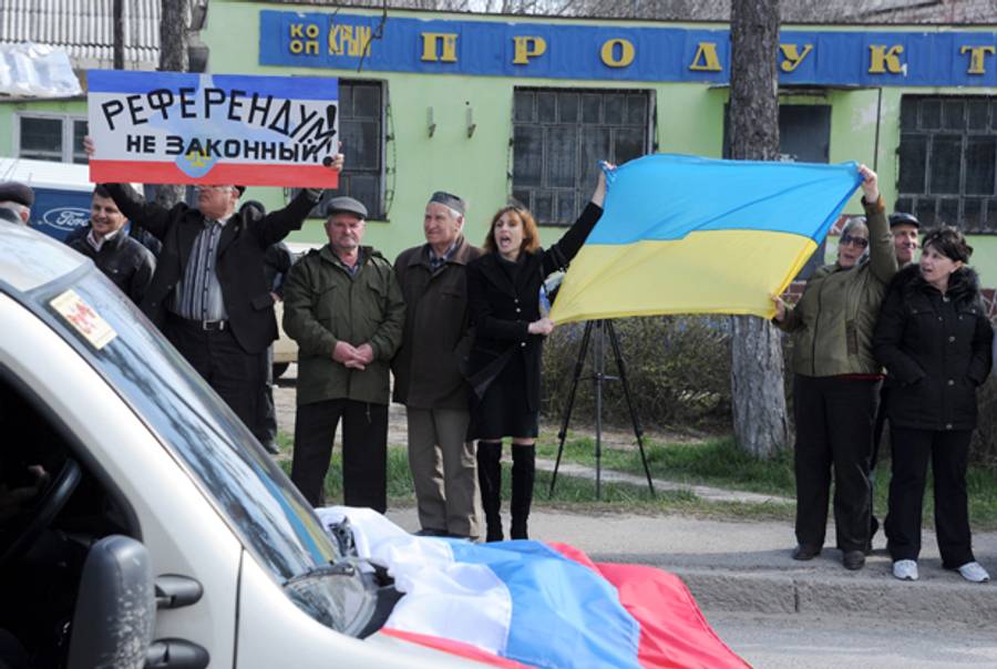 A man holds a sign reading 'Illegal referendum' (L) and women hold a Ukrainian national flag as members of the Crimean Tatar community take part in a demonstration rally in front of a Ukrainian military base in the town of Bakhchisarai, some 40km south of Simferopol, on March 14, 2014, two days before a referendum in Crimea over its bid to break away from Ukraine and join Russia. (VIKTOR DRACHEV/AFP/Getty Images)