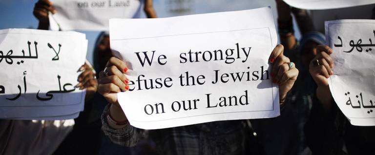 Libyans hold signs during a demonstration against the presence of Jews in Libya and the reopening of the Dar Bishi Synagogue in Tripoli on Oct. 7, 2011.