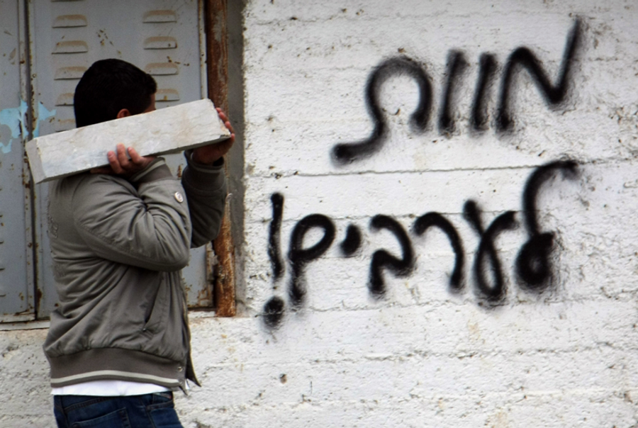 A Palestinian man carries a slab of stone as he walks past graffiti scrawled on the wall at a mason's yard that reads in Hebrew, 'Death to Arabs,' on Feb. 7, 2012, in the village of Al-Lobban Al-Sharqiyeh, southeast of the northern city of Nablus in the Israeli occupied West Bank.