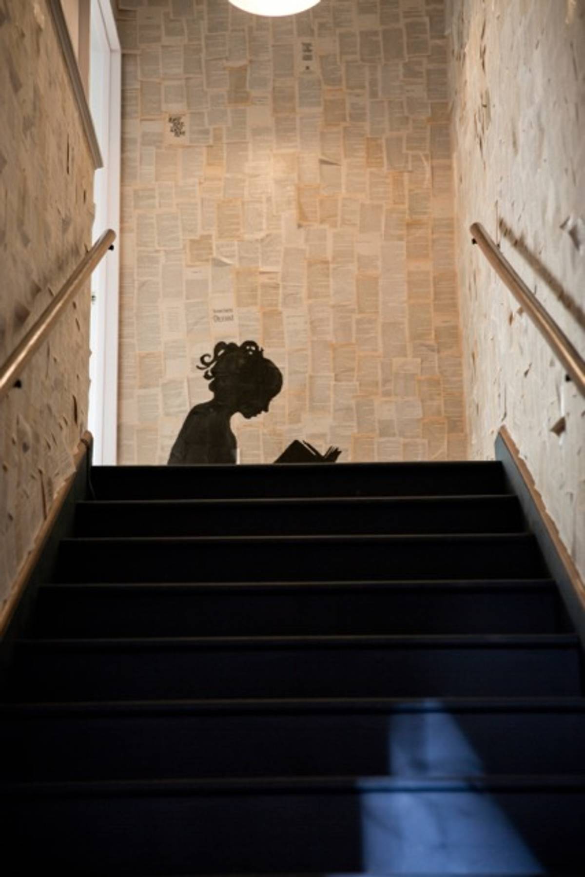 Staircase walls (to used book room) papered in old romance novel pages, with silhouette of reading girl, by Leah. (Image by Jenn LeBlanc)
