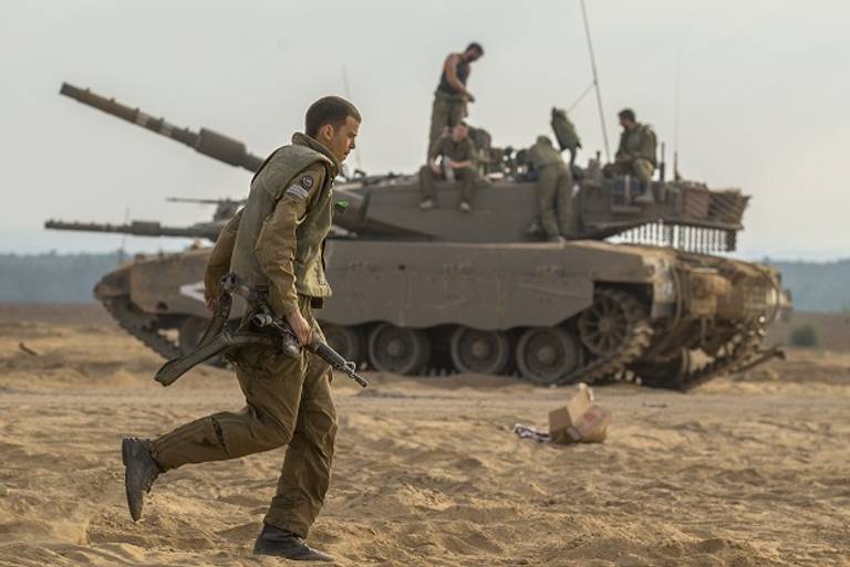 An Israeli soldier runs infront of an Israeli Merkava tank at an army deployment area on the southern Israeli border with the Gaza Strip, on August 1, 2014. (Getty Images)