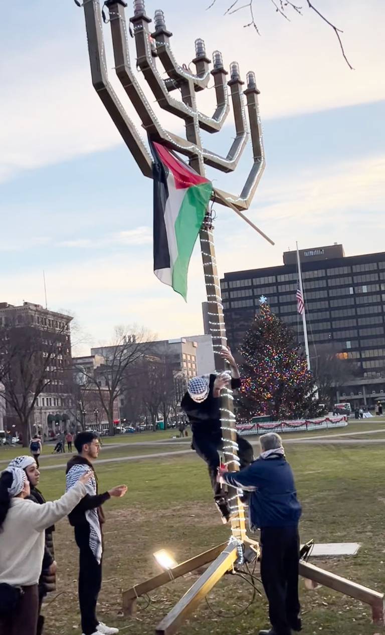A pro-Palestinian demonstrator places a Palestinian flag on a menorah on New Haven Green, Dec. 10, 2023