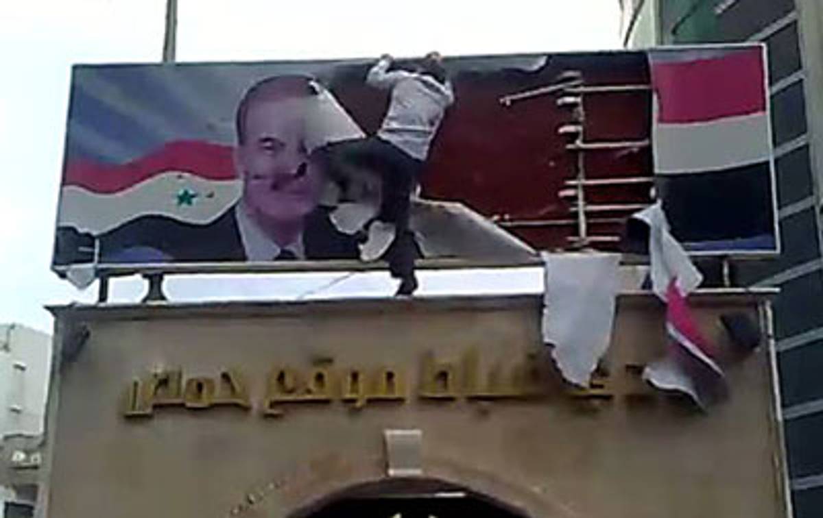 YouTube screen grab obtained by AFP on March 25, 2011 showing a Syrian protester tearing up a poster showing former Syrian president Hafez al-Assad from a banner upon the entrance of a military officers club in the Syrian city of Homs. (AFP/Getty Images)