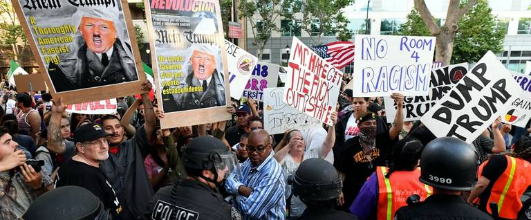Protesters hold up signs against a police skirmish line near where Republican presidential candidate Donald Trump holds a rally in San Jose, California on June 2, 2016. 