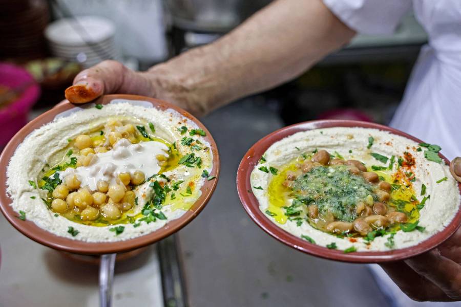 A cook prepares to serve plates of hummus and fava beans to clients at a restaurant in the Old City of Jerusalem, 2022
