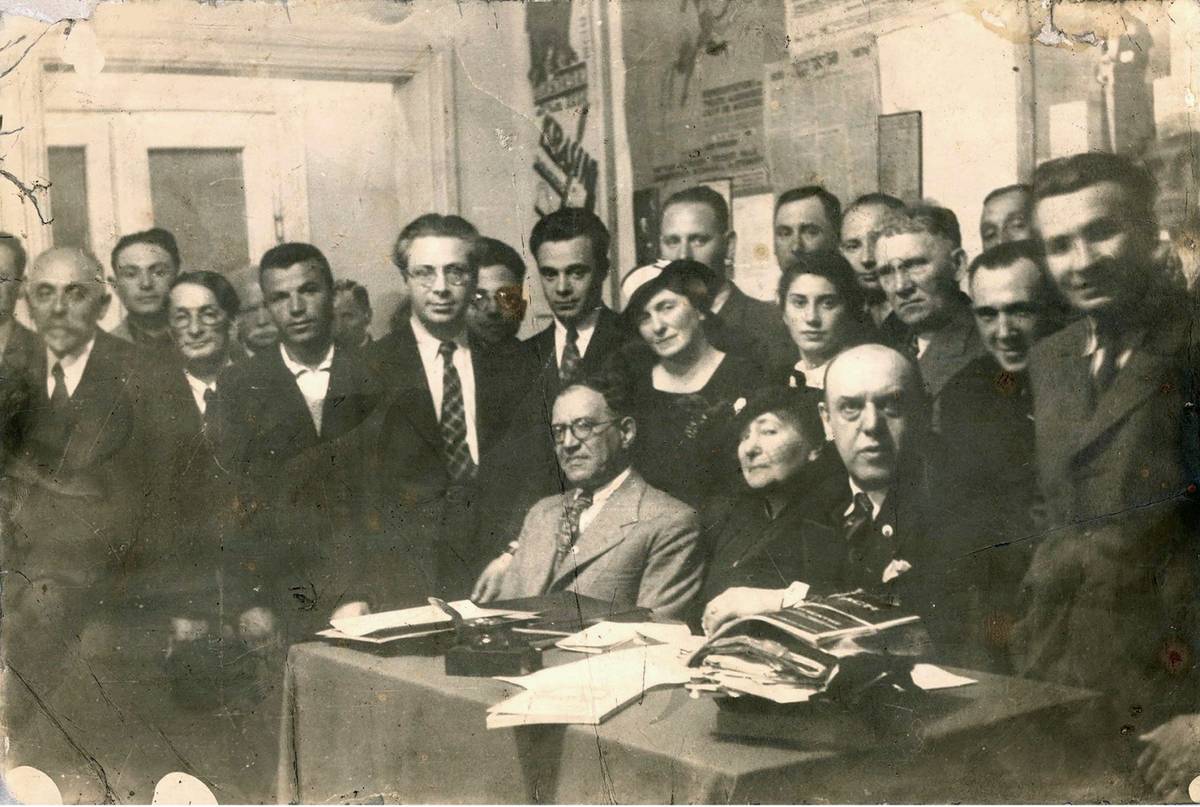 Max Weinreich, in checkered tie and open jacket, standing next to Zalmen Reyzen (seated to his left) and surrounded by 21 aspirants and members of the YIVO personnel and their wives, circa 1938. The young woman standing next to Reyzen’s wife is Uma Olkenitski, director of the Ester-Rokhl Kaminska Theater Museum. The elderly man at the very left is Hirsh Abramowitz, and sitting in the very front next to his wife is David Kaplan-Kaplanski, a YIVO benefactor.